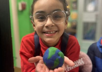 A girl holds out a clay model of the earth.