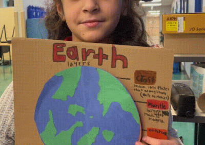 A student opens a cardboard model of the earth to reveal the layers of the earth including the crust, mantle and core.